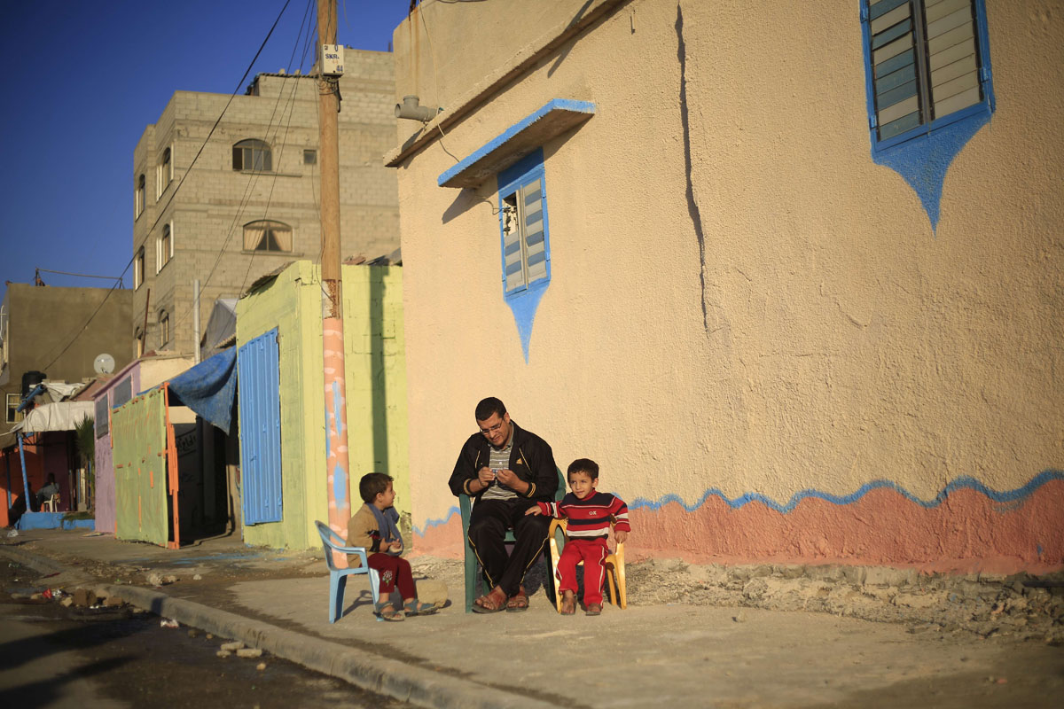 A Palestinian family sit outside their house painted by Palestinian artists in the al-Shati refugee camp in Gaza City, on November 12, 2015, as more than 30 artists take part in a project funded by Padico holding, a limited public shareholding company traded on the Palestine Exchange (PEX). AFP PHOTO / MOHAMMED ABEDMOHAMMED ABED/AFP/Getty Images ORG XMIT: